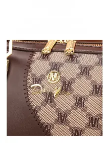 Detail of brown leather stitching and golden M logo pendant on the crossbody bag