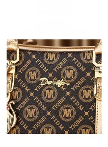 Gros plan du sac à main en cuir marron à motifs avec logo doré et pendentif chat