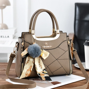 Close-up of brown textured leather handbag with gold metal handles and pompom charm