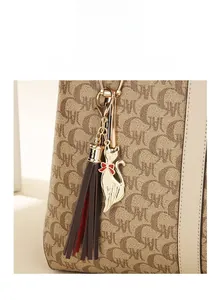 Detail of a golden cat charm with red-brown tassels on a textured tote handbag