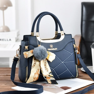 Detail of dark blue handbag with lychee texture, silk scarf, and plush ball charm on a desk