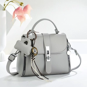 Light gray pebbled leather handbag with adjustable strap and teddy bear charm accessory