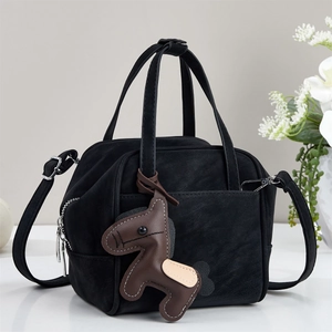 Detail of black suede tote bag with brown horse charm and versatile shoulder strap