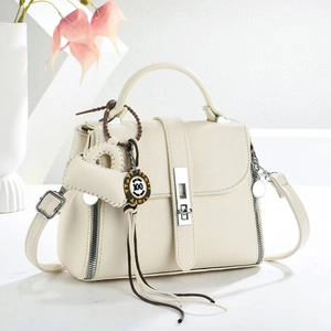 Detailed macro view of cream textured leather handbag with silver rotary lock and mini charm