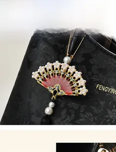 Dettaglio di un ciondolo a ventaglio dorato con perle e nappe su una borsa stile New Chinese