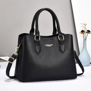 Detail of black lychee grain leather handbag with gold hardware and shoulder strap