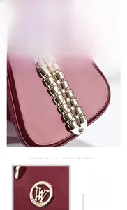 Detail of burgundy patent leather bag with golden rivets and fashion logo plate