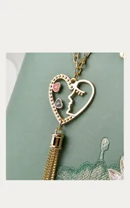 Macro detail of golden metal heart pendant with tassels on embroidered leather bag