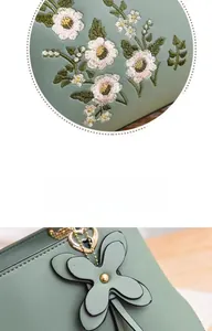 Detail of floral embroidery and heart metal pendant on grey-green cross-body bag
