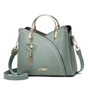 Detail view of green handbag showing gold metal handle and pearl heart tassel charm