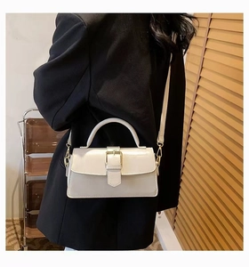 Cream patent leather handbag with gold metal accents shown on a black suit model
