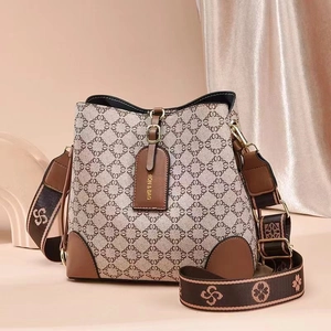 Nahaufnahme einer beigen Monogramm-Beuteltasche mit braunem Lederbesatz und breitem Gurt