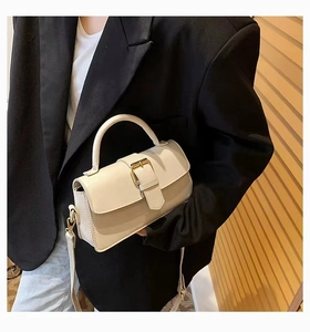 Detail of a creamy leather handbag with golden buckle held by a model in a black blazer