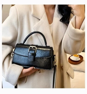 Detail of a black pleated PU leather handbag with metallic buckle on a tweed coat