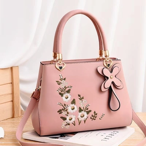 Pink faux leather handbag with floral embroidery and golden hardware in an elegant setting