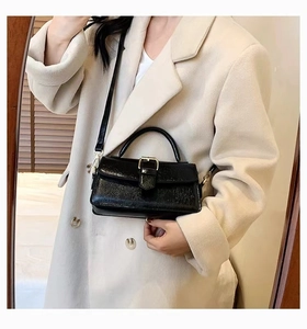 Detail of black wrinkled texture handbag with gold buckle on a beige coat background