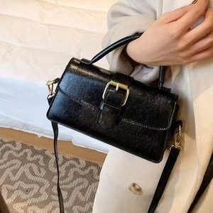 Detail of vintage black patent leather handbag with gold buckle and detachable shoulder strap
