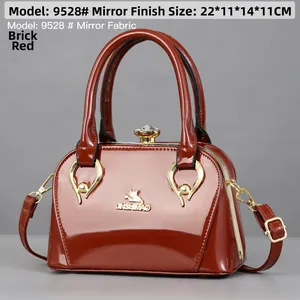 Detailed view of brick red mirror patent leather handbag with rhinestone clasp and gold logo