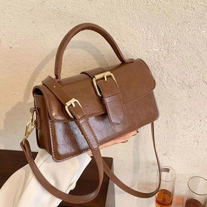 Close-up of vintage brown leather handbag with golden buckles and adjustable strap