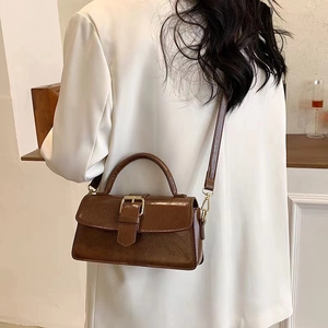 Vintage dark brown faux leather handbag with golden buckle worn on a white suit