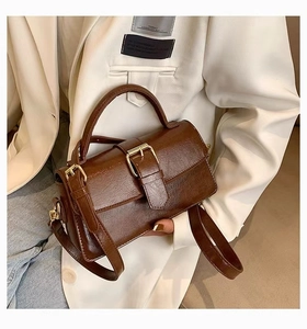 Detail of dark brown glossy leather handbag with vintage metal buckle and top handle