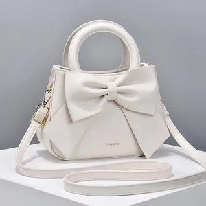 Détail d'un sac à main beige orné d'un grand nœud et d'un logo métallique doré