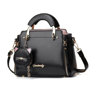 Sac à main noir en cuir avec fermetures dorées et pendentif chat sur fond blanc
