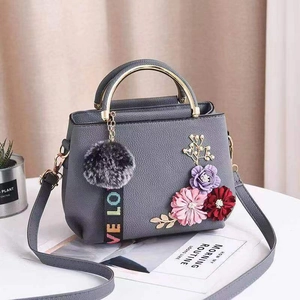 Graue Handtasche mit Blumenstickerei, Pelzanhänger und Schultergurt in einer Wohnzimmerszene