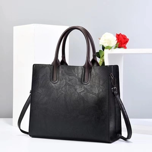 Bolso tote negro de moda con textura plisada y asas marrones sobre un soporte blanco