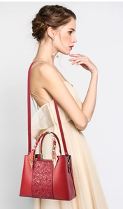 Detail of red leather handbag with floral embossing and silk scarf wrap on the handle