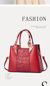 Detail of red cowhide handbag with floral embroidery and silk scarf handle decoration