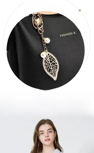 Détail d'un sac à main en cuir noir avec pendentif feuille dorée et perles blanches