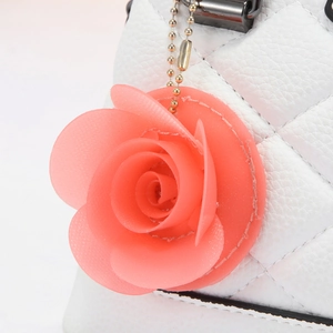 Detail of pink resin rose pendant charm on white quilted evening shell bag with gold chain