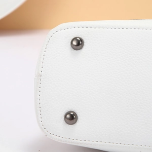 Macro shot of white leather handbag base with protective metal studs and fine stitching