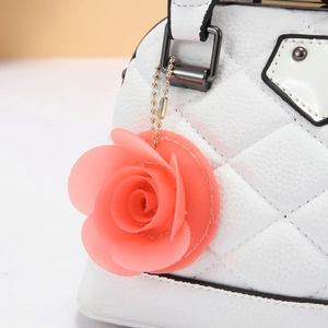 Detailed close-up of pink rose charm on white quilted leather bag with gold chain