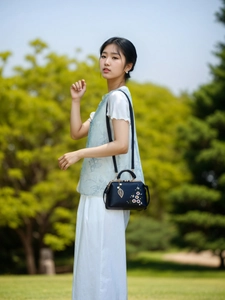 Detailed embroidery on vintage navy handbag with metal leaf charm and clasp closure