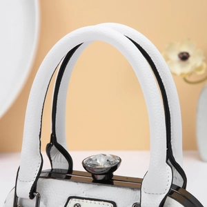 Detail of white quilted handbag featuring a luxury crystal lock and black metal frame