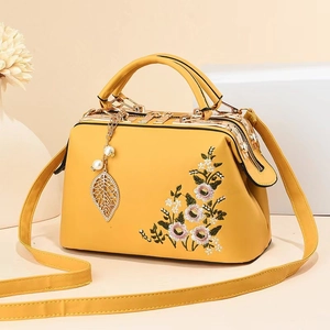 Detailed embroidery of pink flowers on a yellow leather doctor bag with metal clasp
