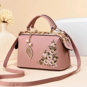 Detail of pink leather handbag featuring floral embroidery and golden leaf pendant