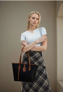 Close-up of black pebble leather tote bag featuring contrast brown handles and brand tag