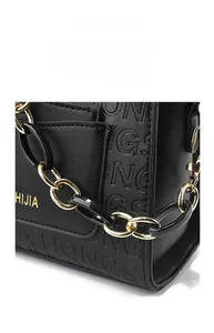 Détail d'un sac à main en cuir noir avec une chaîne épaisse en métal doré et acrylique