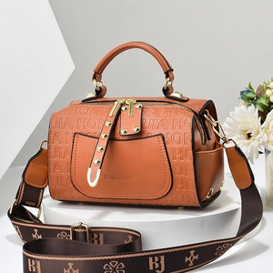 Brown leather embossed pillow bag with patterned wide strap on a white display stand