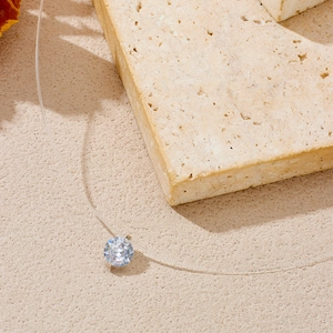 Macro shot of a single diamond pendant on a transparent fishing line necklace over stones