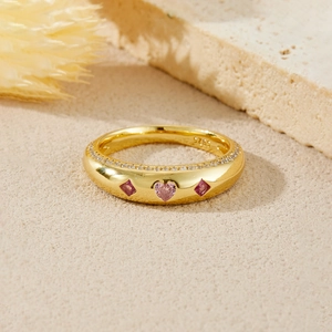 Macro shot of S925 silver gold heart ring with pink and red stones on sand stone