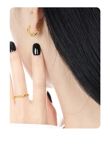 Detail of gold geometric chain earrings and textured ring on a person with black nails