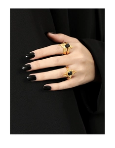 Detail of gold irregular lava rings with square black gemstone on fabric background