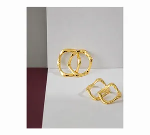 Makroaufnahme minimalistischer goldener Wellenohrringe mit flüssiger Metallstruktur im Licht