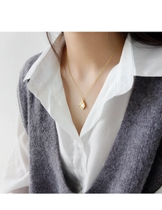 Primer plano de un collar dorado con colgante de textura irregular sobre una camisa blanca