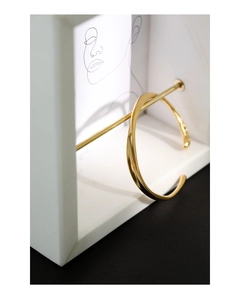 Close-up of a minimalist golden twisted open cuff bracelet on a white display stand