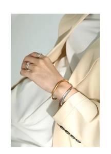Polished silver and gold open bracelets styled with matching chunky rings on a model